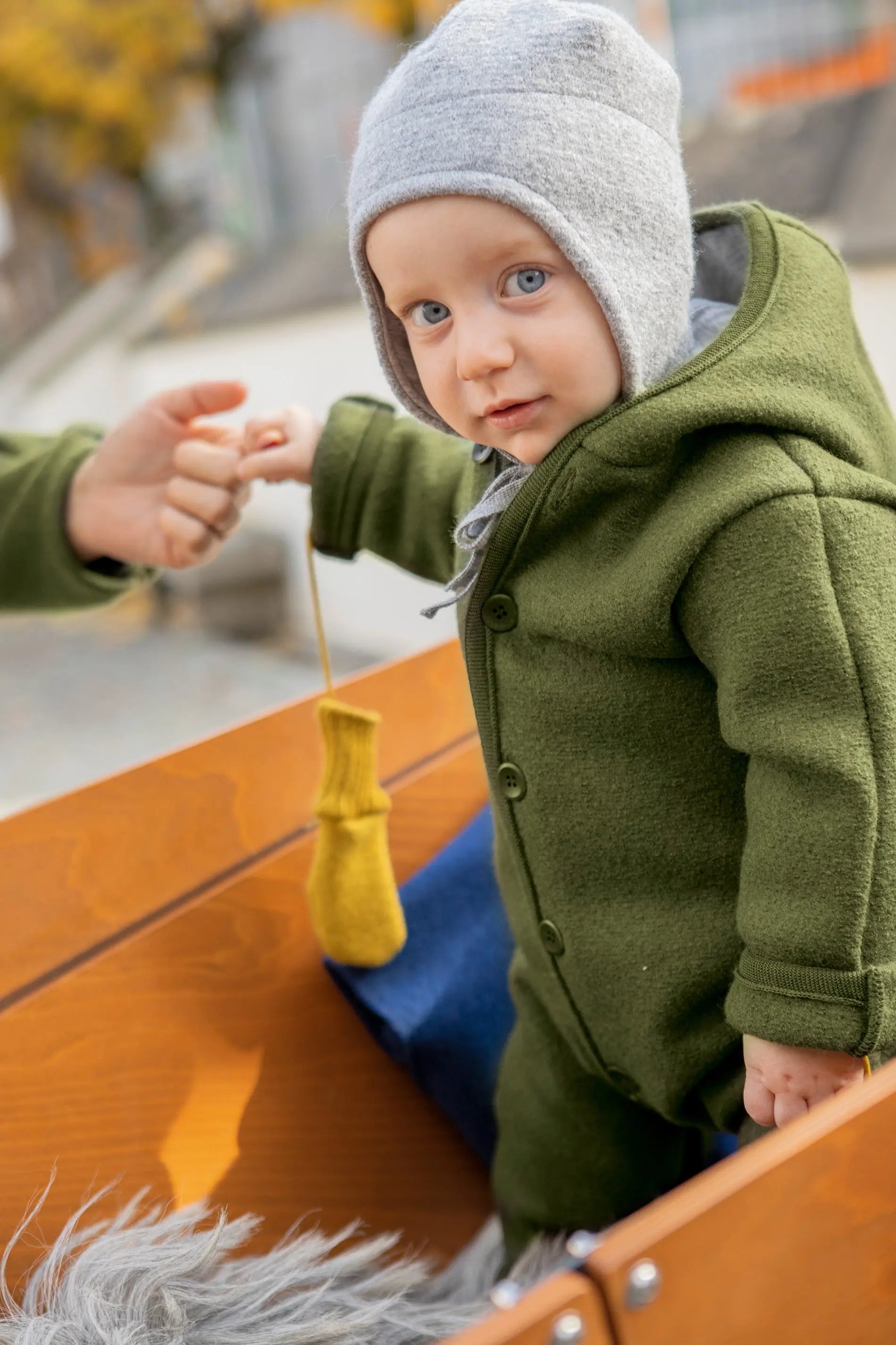 Baby in olive boiled wool bunting holding on to a hand