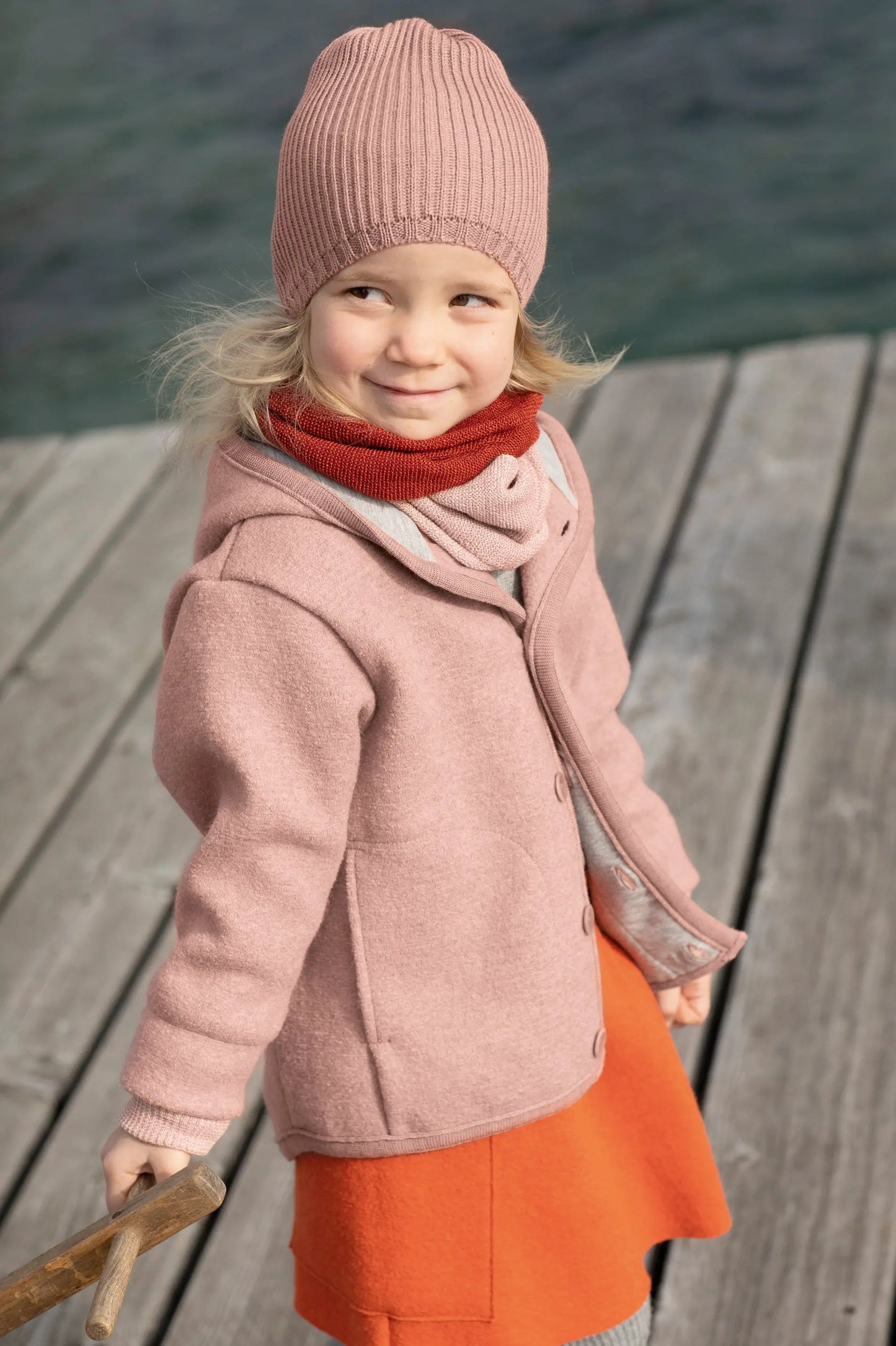 Girl in rosé boiled wool coat on a dock of a bay 