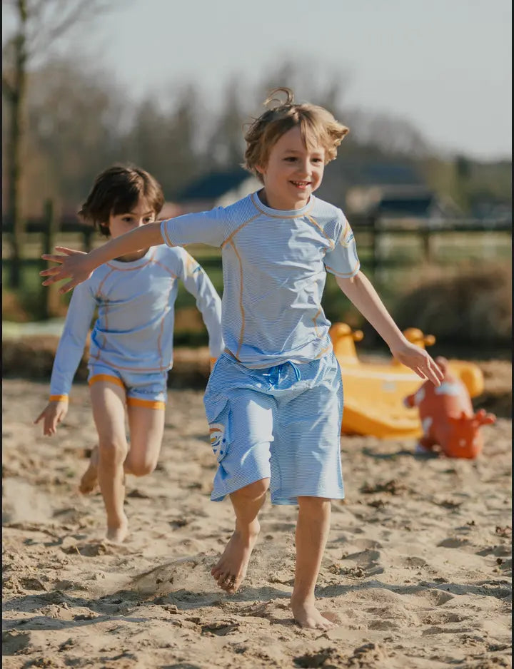 Two boys in swim trunks running at the beach